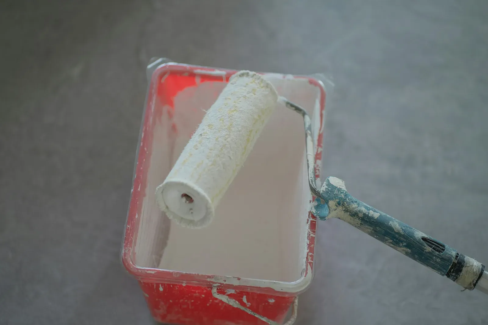 A paint-stained roller resting in a tray of white paint