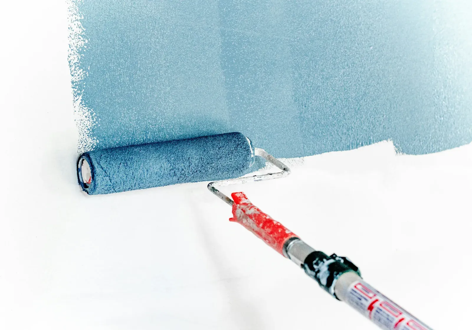 A paint roller spreading blue paint across a white wall