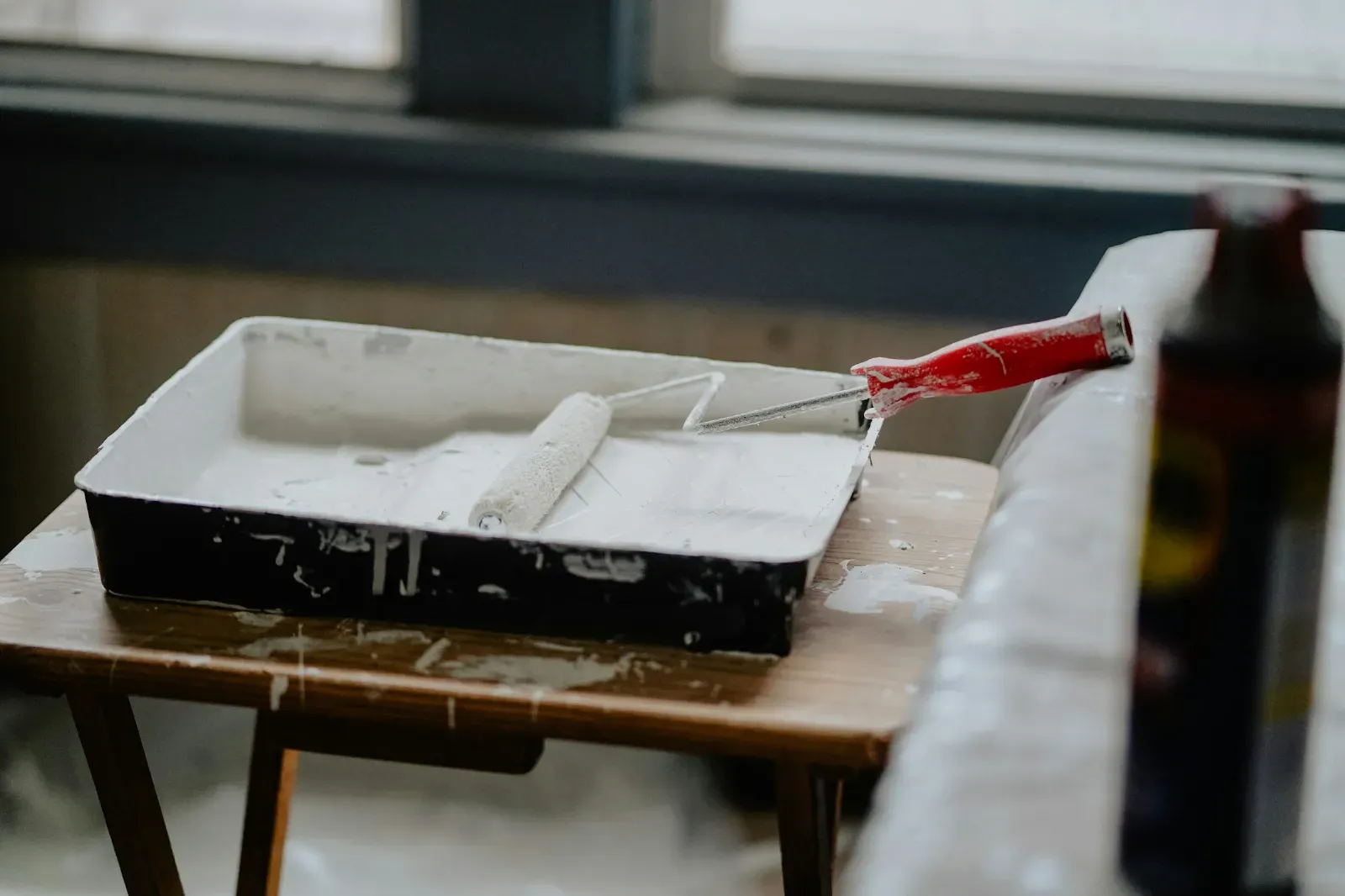 A paint tray and roller resting on a stand by a window