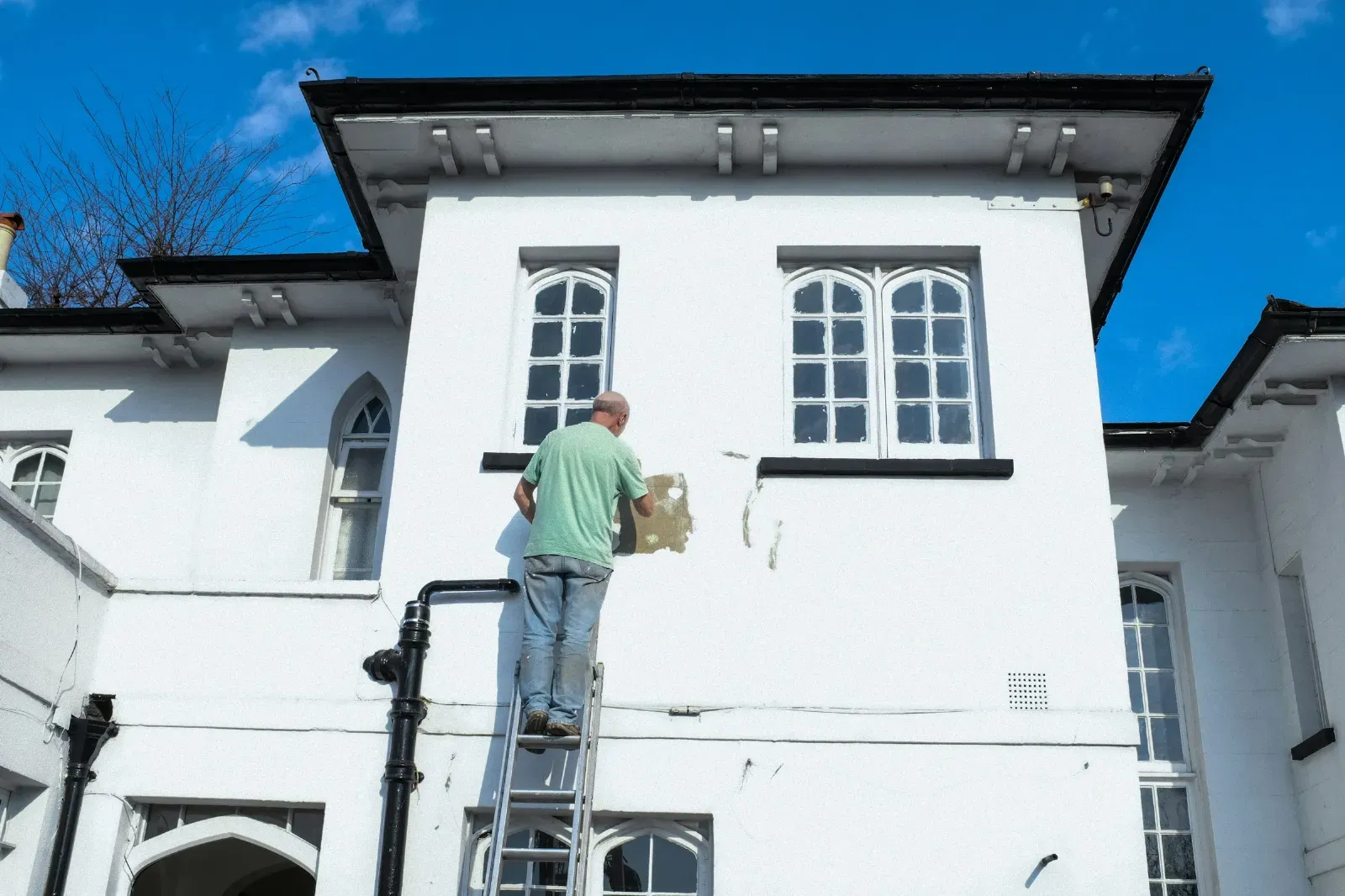 A worker on a ladder repairing an exterior wall