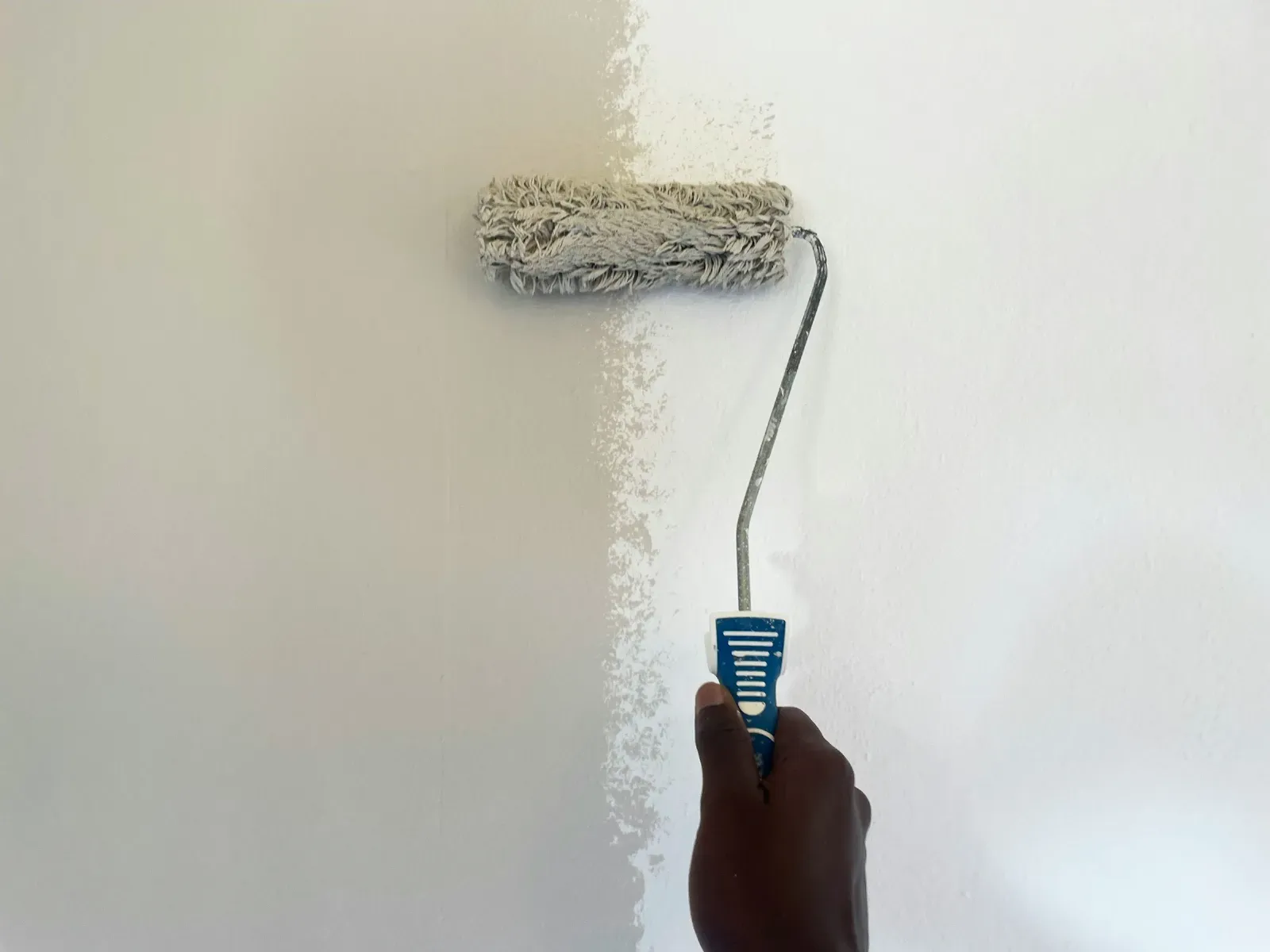 A hand rolling fresh white paint over a wall